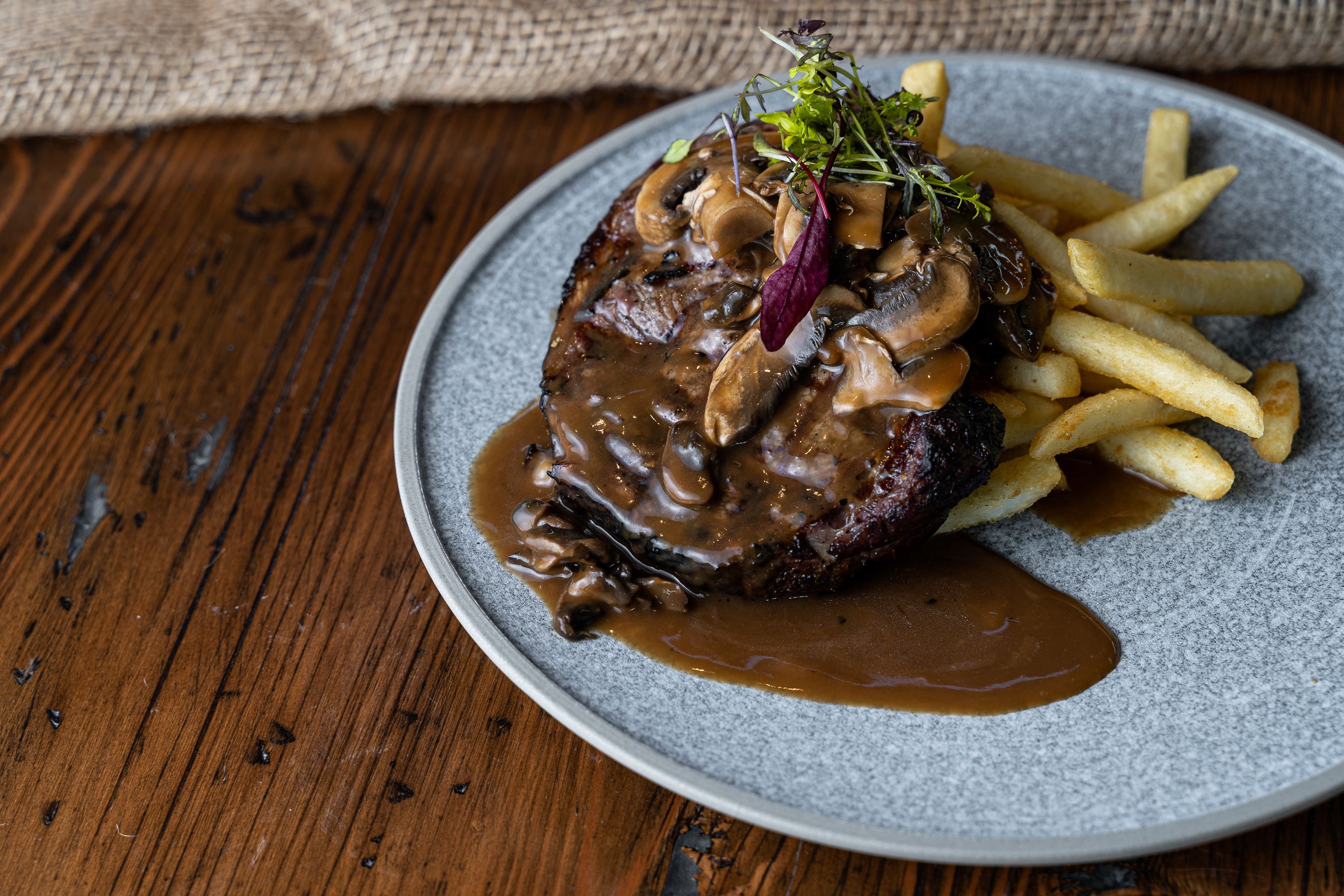 A plate with a steak topped with mushrooms and gravy, accompanied by French fries.