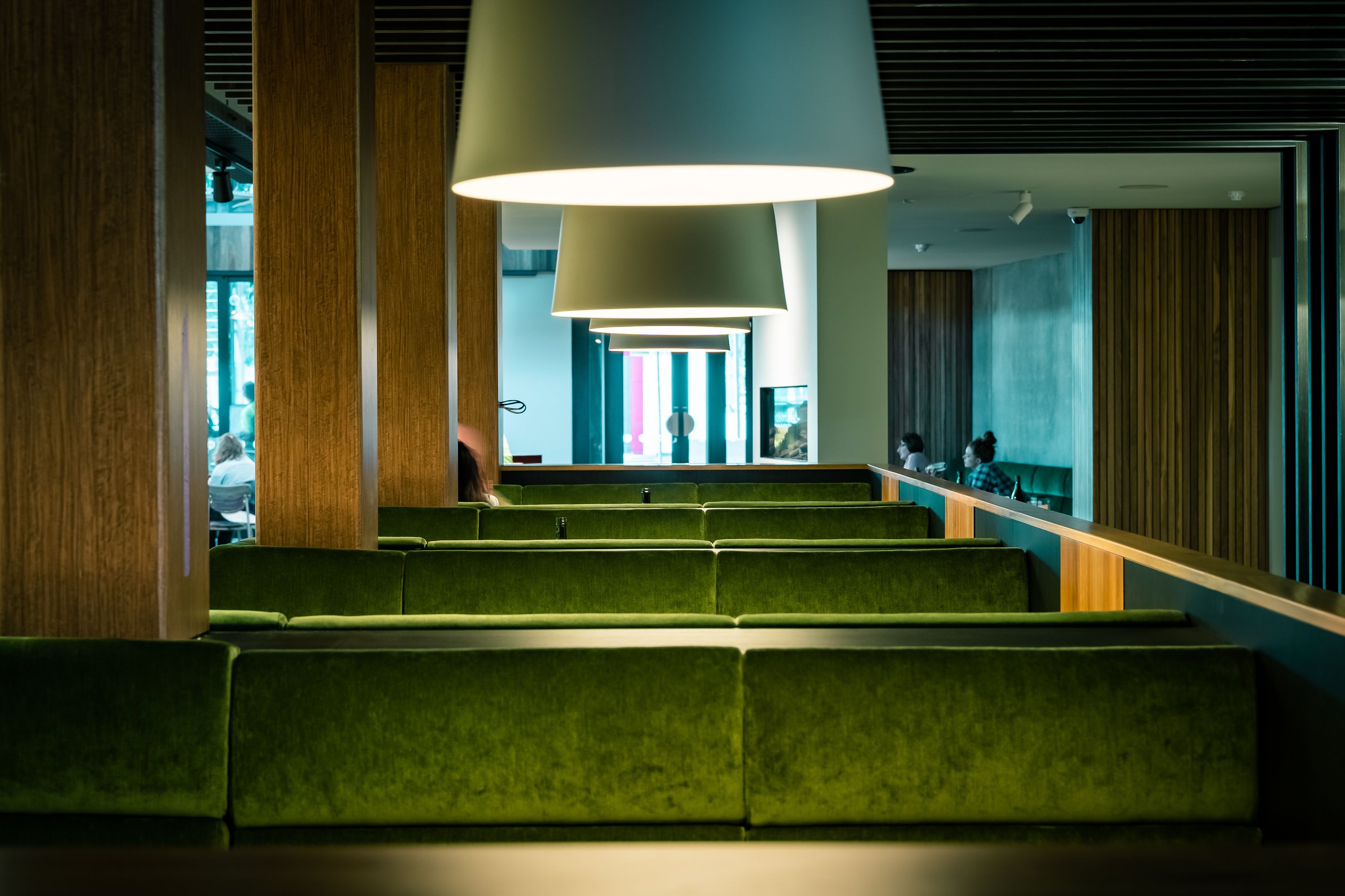 Un escalier moderne agrémenté de sièges rembourrés verts, d’un grand lampadaire suspendu et offrant une vue sur le hall d’entrée.