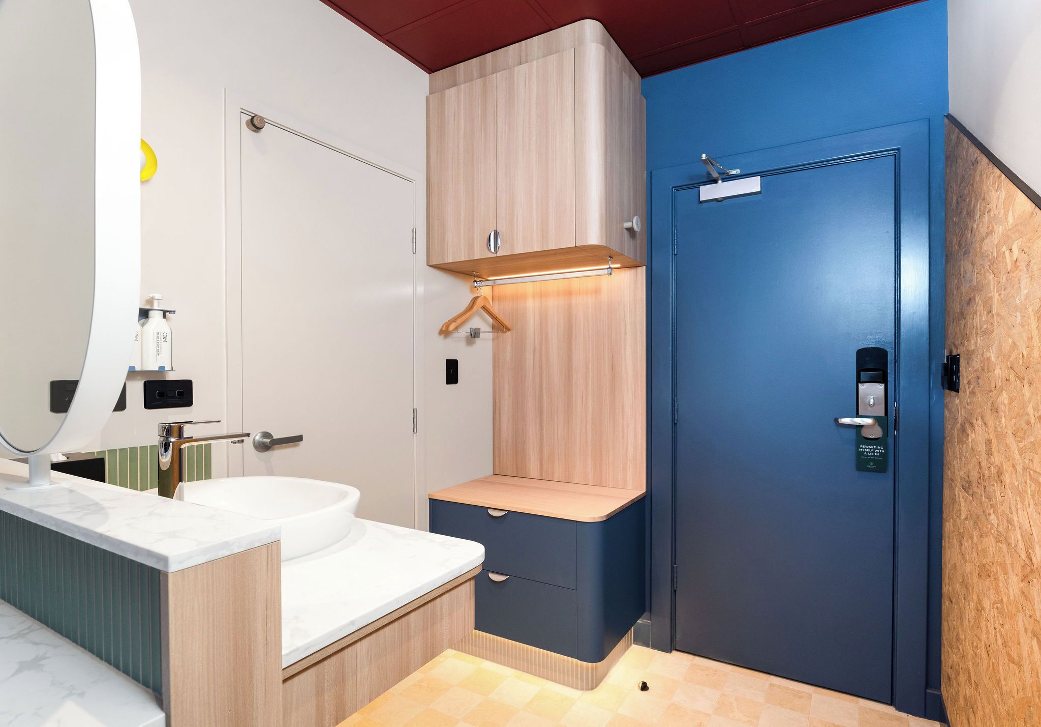 Un baño moderno con un lavamanos blanco, armarios de madera y una puerta azul.