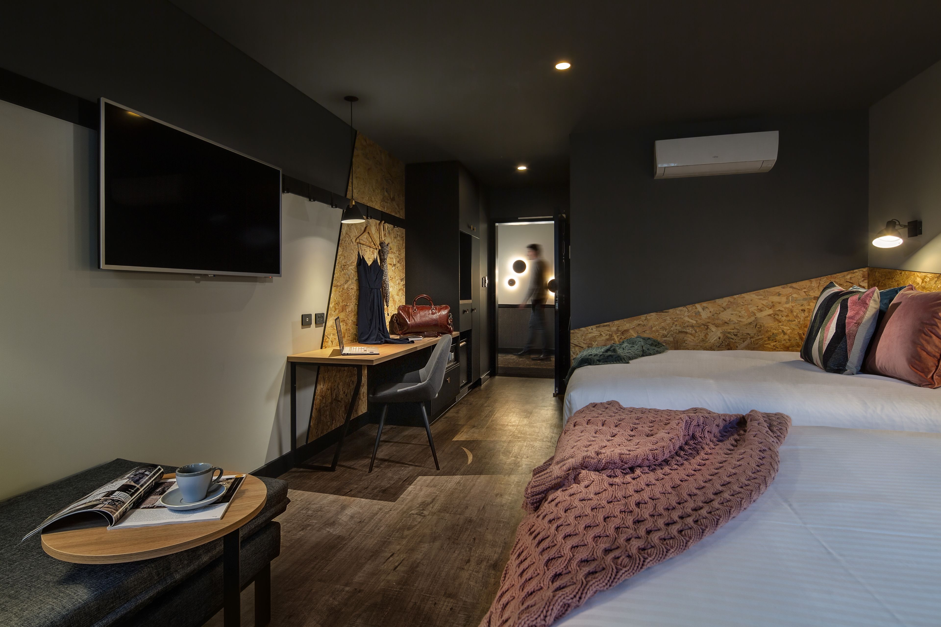 Una habitación de hotel moderna con cama, escritorio, silla, televisor y aire acondicionado instalado en la pared.
