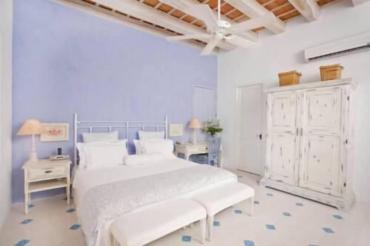 Une chambre à coucher comprenant un lit, des tables de chevet, une armoire et un ventilateur de plafond.