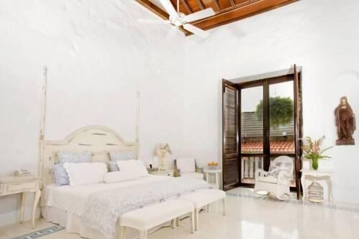 Une chambre à coucher comprenant un lit, des tables de chevet, un banc, une commode, une statue et une vue à travers une porte vitrée.