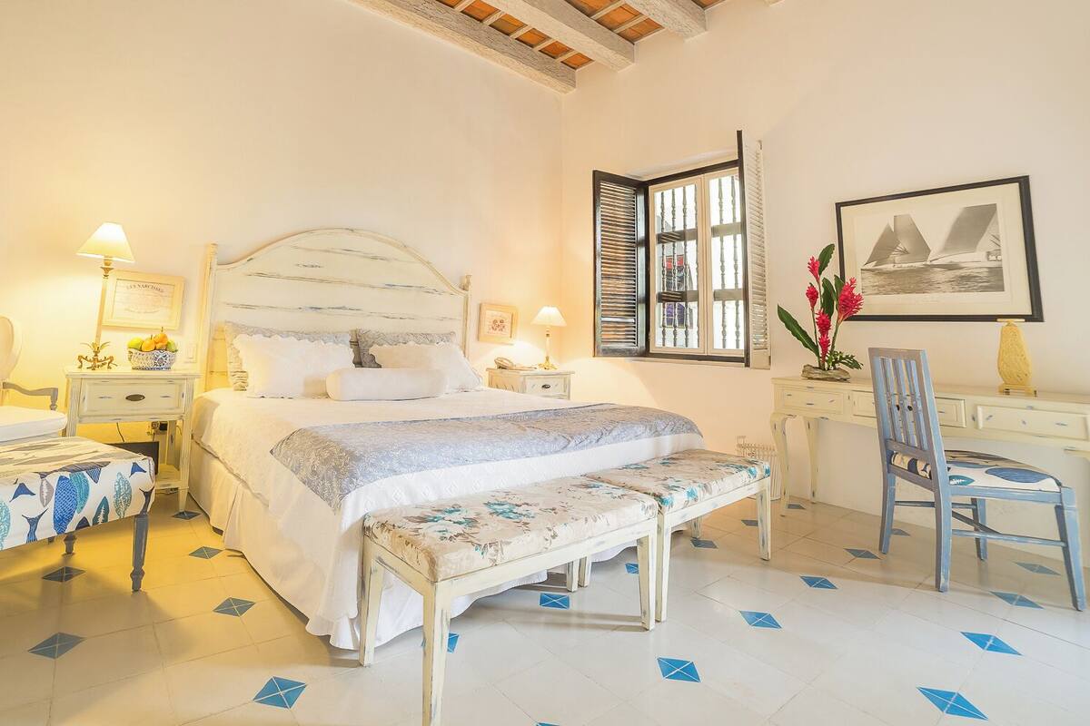 Une chambre à coucher comprenant un lit, des tables de chevet, un bureau, une chaise et une fenêtre avec des volets.
