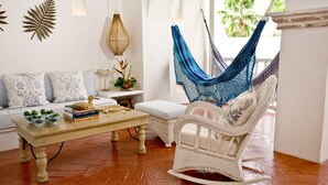 Ein Zimmer mit einem weißen Sofa, einem Holztisch, einem Schaukelstuhl aus Weidengeflecht, einer Hängematte und einer Wanddekoration.
