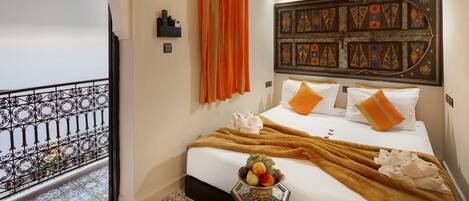 A hotel room with a bed, orange curtains, a decorative headboard, and a fruit bowl on the nightstand.