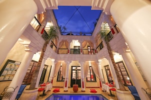 Un área de piscina interior lujosa, con una fuente central, rodeada de columnas y plantas en macetas.