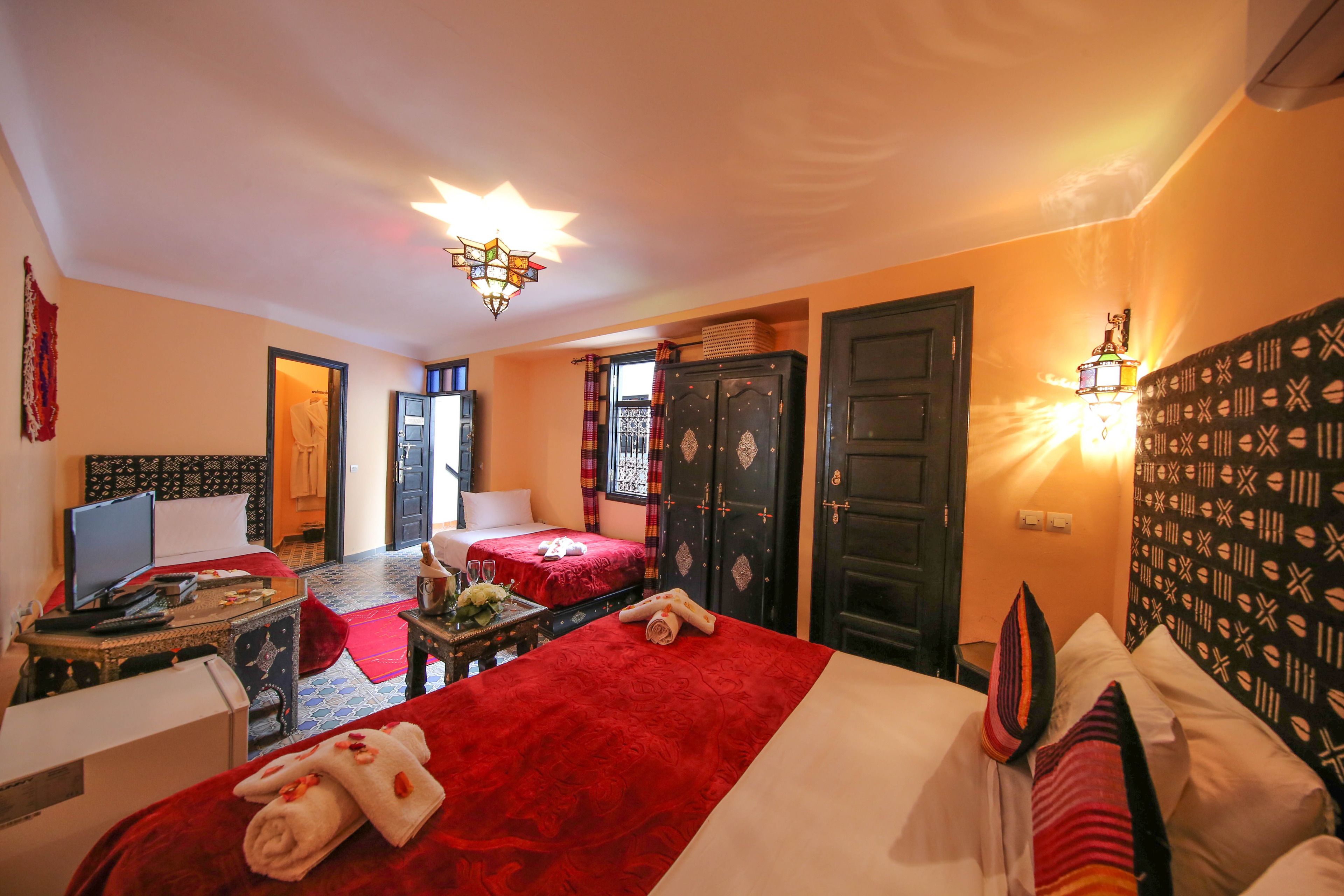 Une chambre d’hôtel avec un grand lit, un bureau avec un ordinateur, une télévision et une petite table sur laquelle est posé un vase de fleurs.