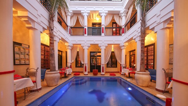 A hotel lobby with a central pool, multiple dining areas, and a balcony with red lanterns. - Riad Africa (Marrakech)
