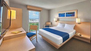 A hotel room with a bed, desk, chair, and a view of the city.