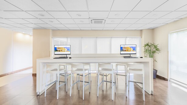 A modern reception area with a long reception desk, multiple chairs, two monitors, and a potted plant.