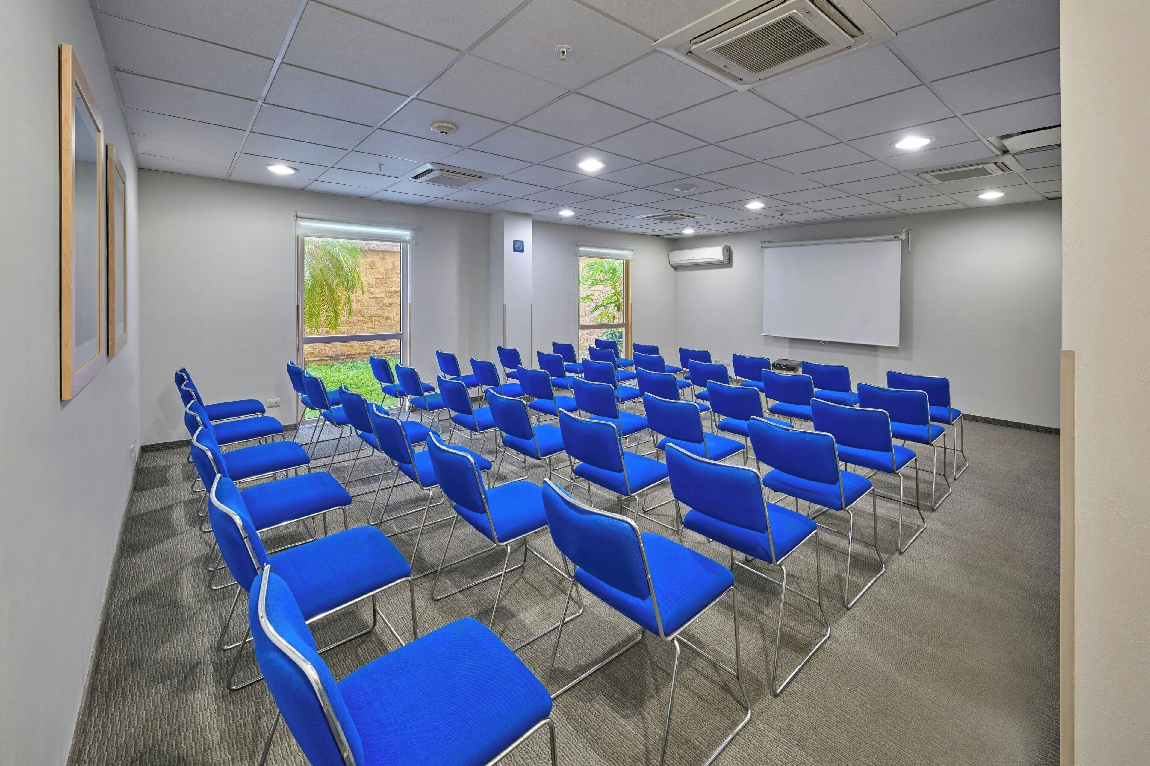 A conference room with rows of blue chairs, a whiteboard, and a projector screen.