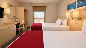 A hotel room with two beds, a desk, a chair, a mirror, and a window with a city view.