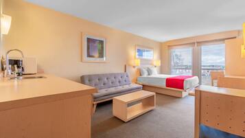 A hotel room with a sofa, a bed, a desk, and a view of the outside.