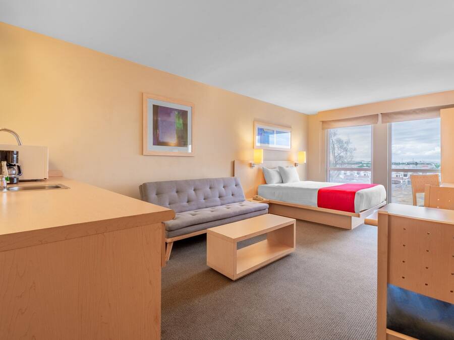 A hotel room with a sofa, a bed, a desk, and a view of the outside.