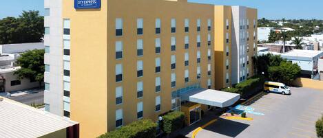 Un hotel de varios pisos con fachada amarilla, un acceso cubierto y un estacionamiento con plazas reservadas para discapacitados.