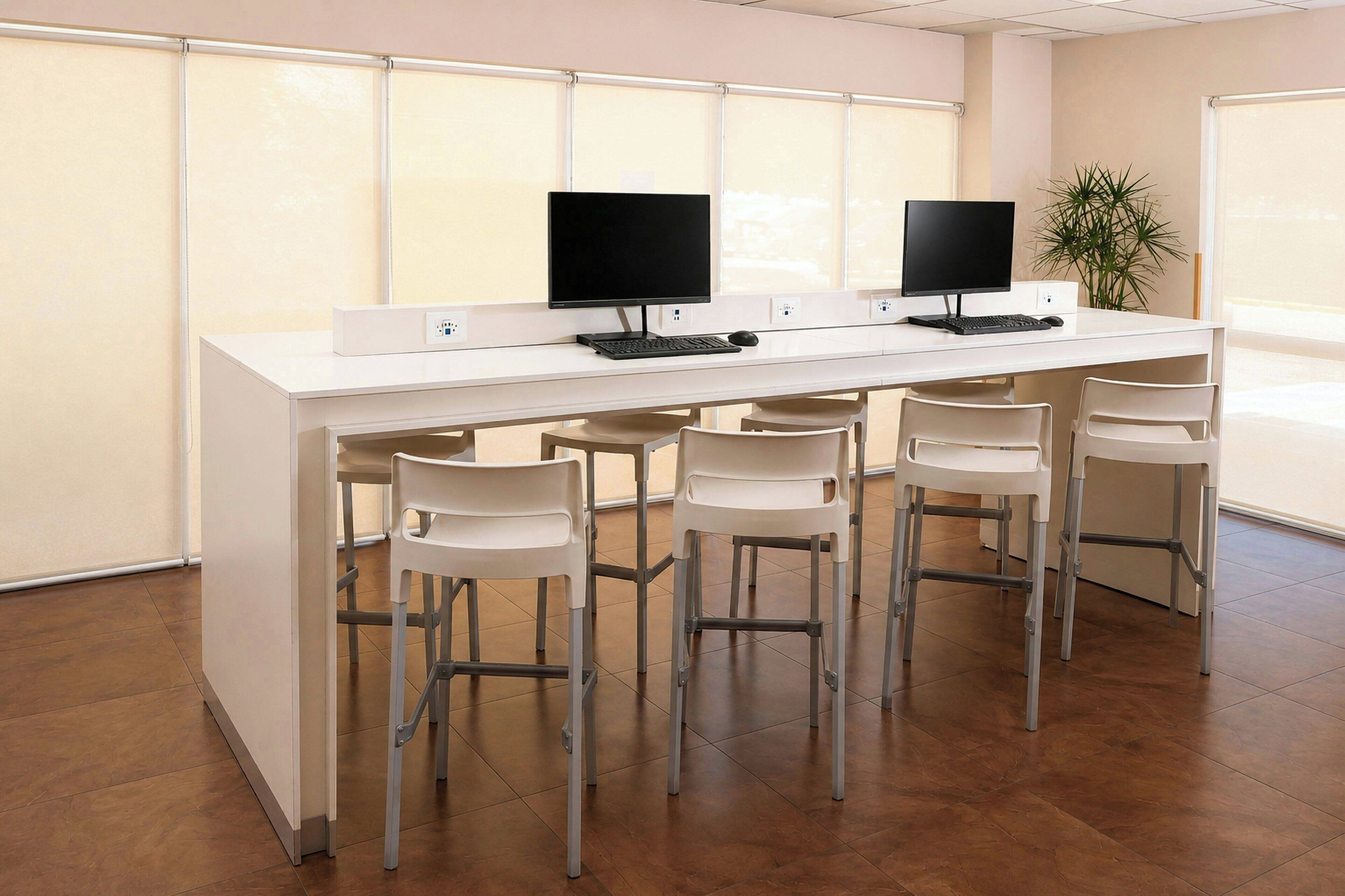 Een modern kantoor met twee bureaus, elk met een computermonitor, toetsenbord en muis. Er staan vier witte stoelen bij de bureaus.