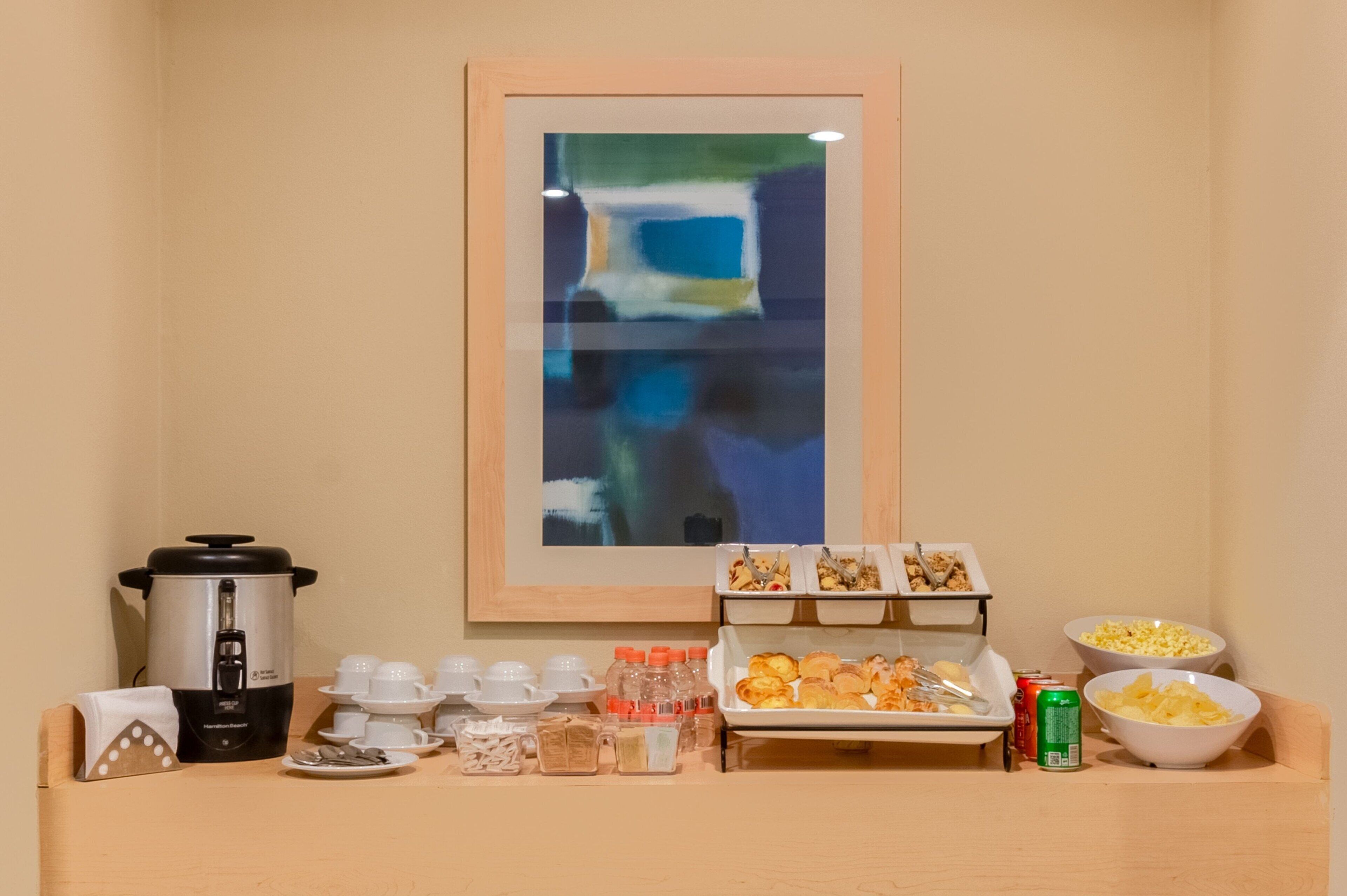 A breakfast buffet setup with a coffee maker, cups, condiments, and food items.