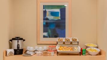 A breakfast buffet setup with a coffee maker, cups, condiments, and food items.