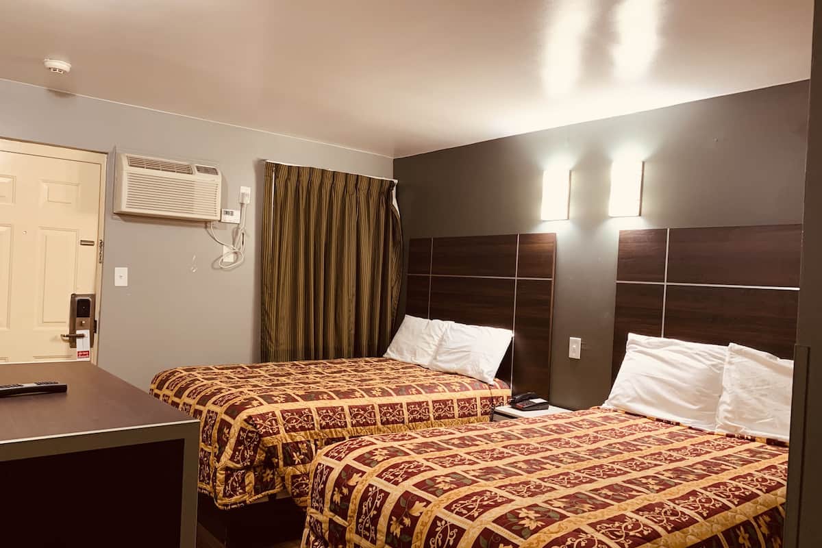 A hotel room with two beds, a desk, an air conditioning unit, a door, and a curtain.