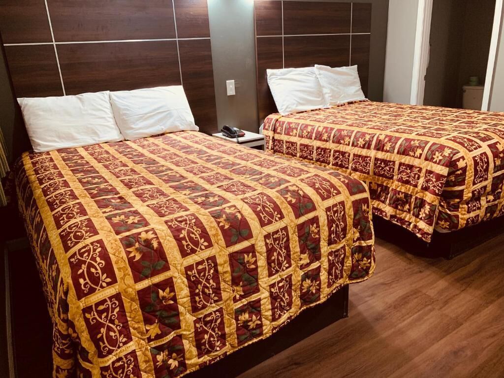 Two beds with patterned quilts, a wooden headboard, and a bedside table with a phone.