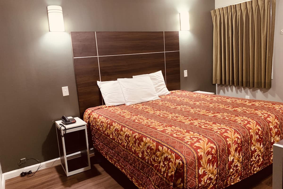 A hotel room with a large bed, a bedside table with a lamp, and a power outlet.