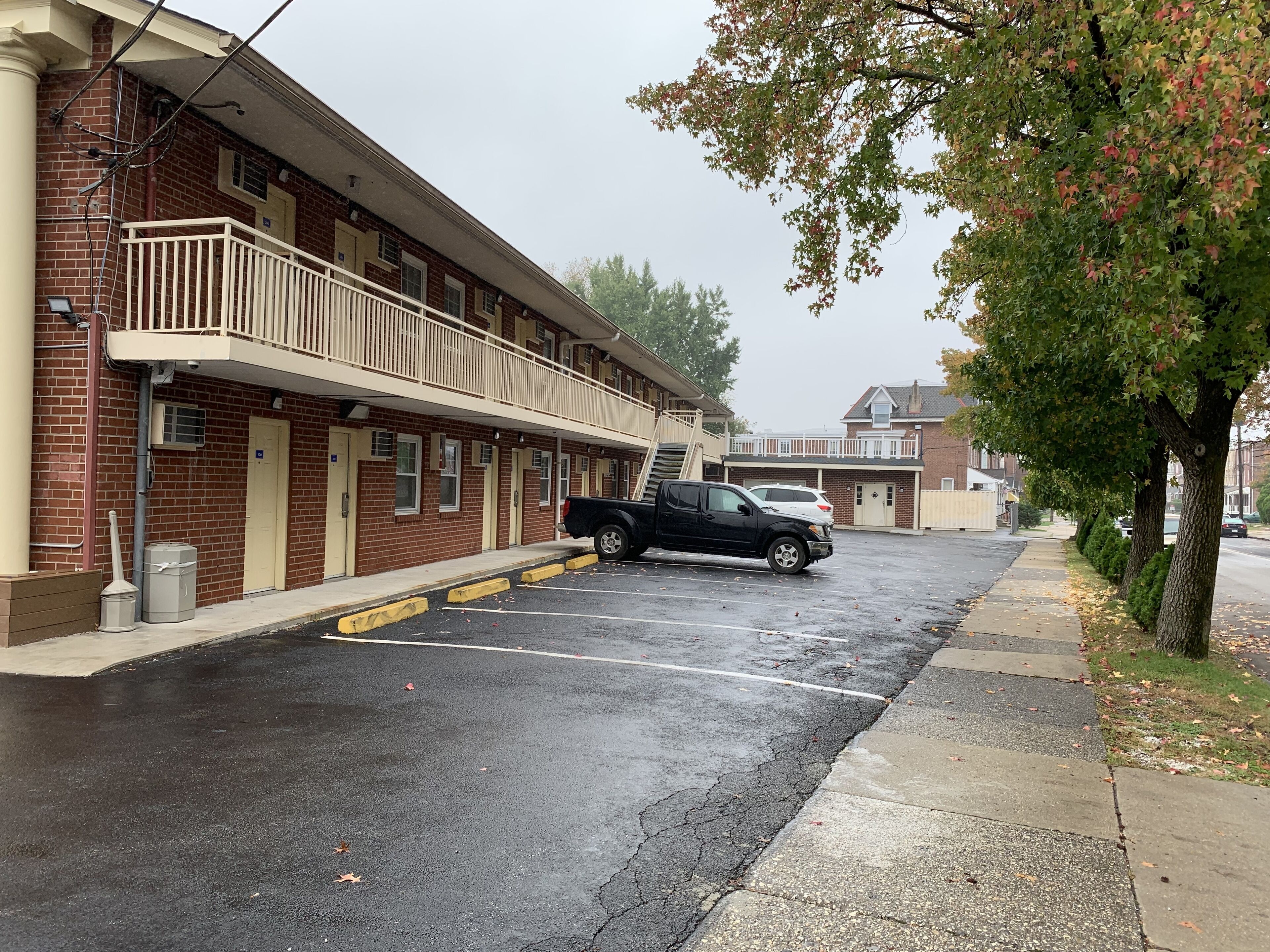 A multi-story motel with a brick facade, a covered balcony, and a parking lot with a black pickup truck.
