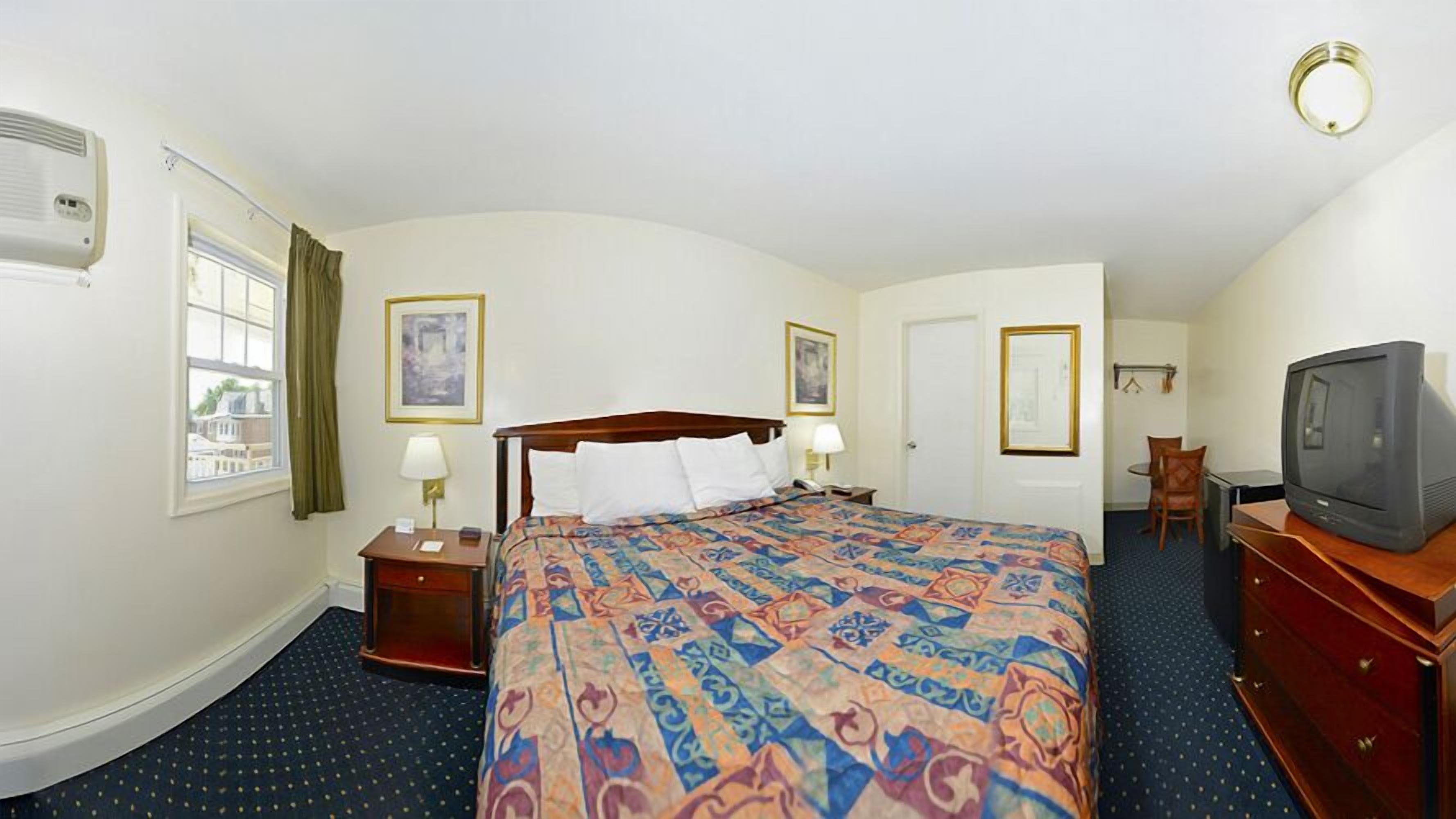 A hotel room with a bed, bedside tables, a desk with a chair, a television, and a window with curtains.