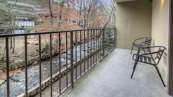 Ein Balkon mit Blick auf einen Bach und Bäume, einem Metallgeländer und zwei Metallstühlen.