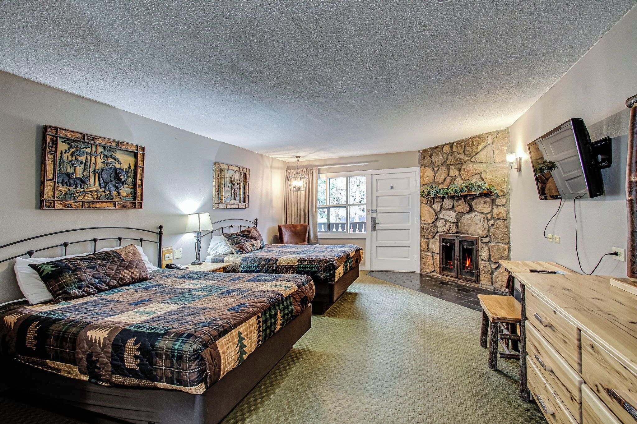 A bedroom with two beds, a stone fireplace, a television, and a desk.
