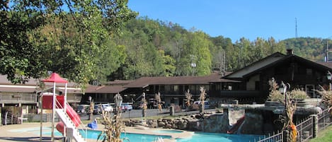 A pool area with a slide, a red canopy, and a building with a balcony in the background.