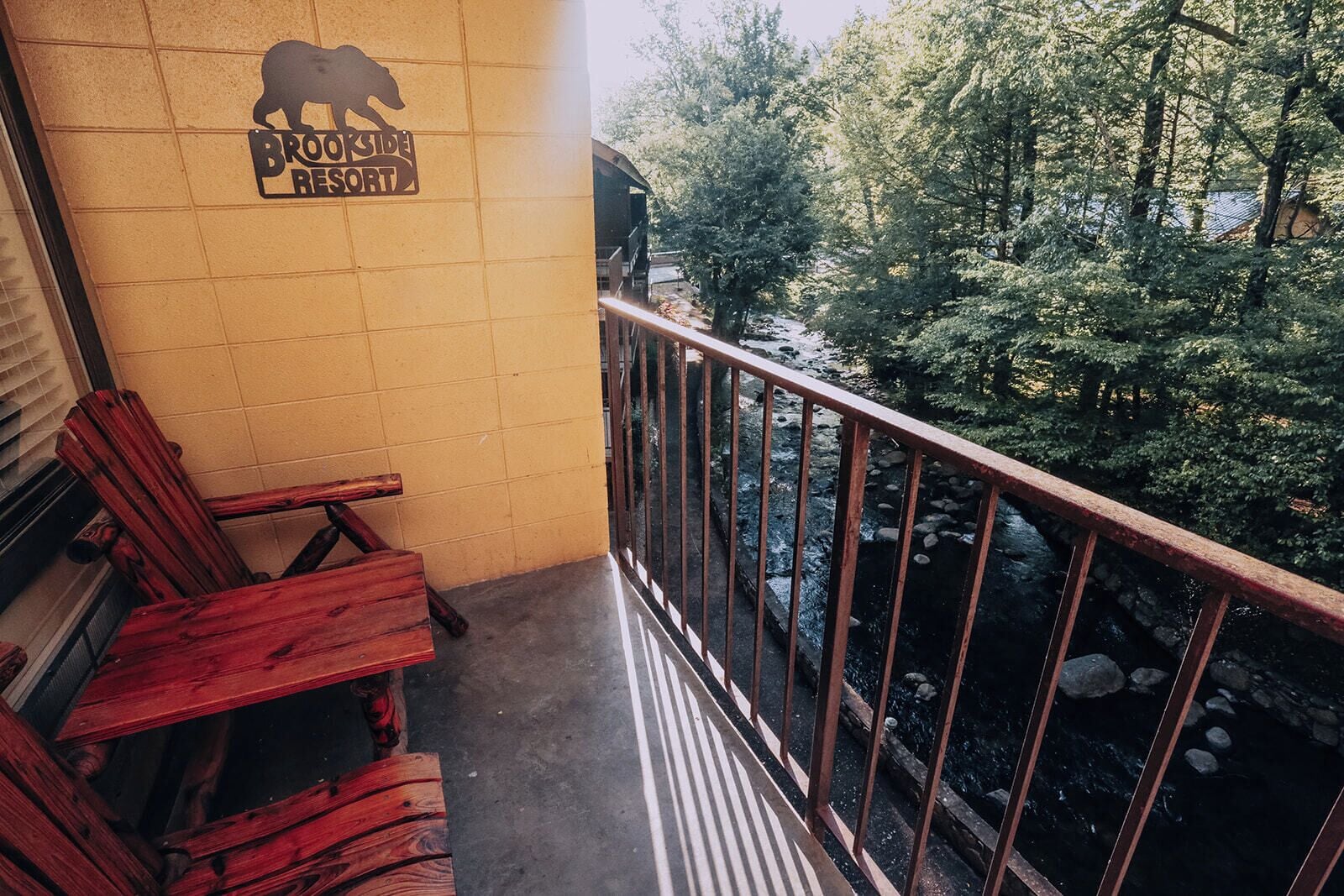 A balcony with a view of a stream and trees, a sign for Brookeside Resort, and wooden chairs.