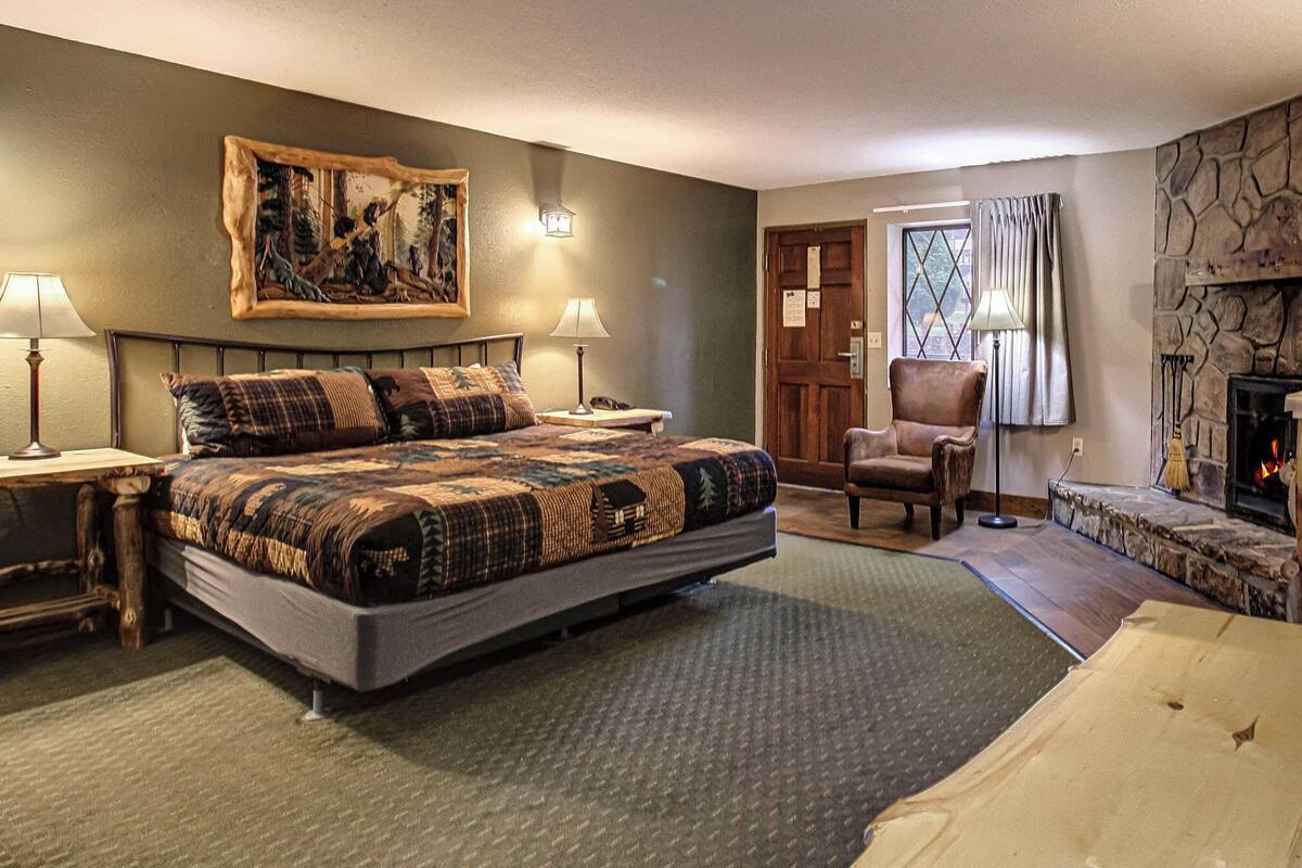 A bedroom with a large bed, a chair, a fireplace, and a painting on the wall.