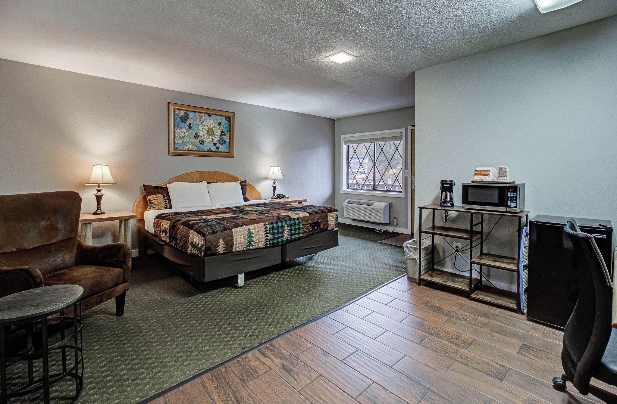 A hotel room with a bed, a chair, a desk with a computer, a coffee maker, and a window.