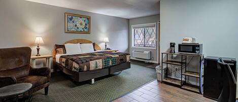 A hotel room with a bed, a chair, a desk with a computer, a coffee maker, and a window.