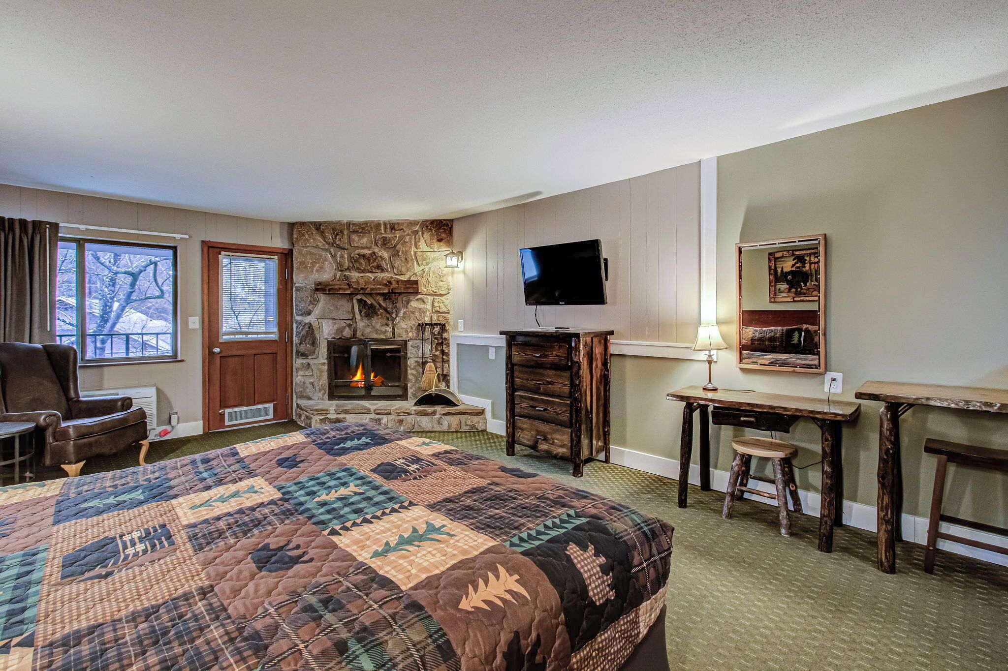 Une chambre d’hôtel avec un grand lit, une cheminée en pierre, une télévision et un bureau avec un tabouret.