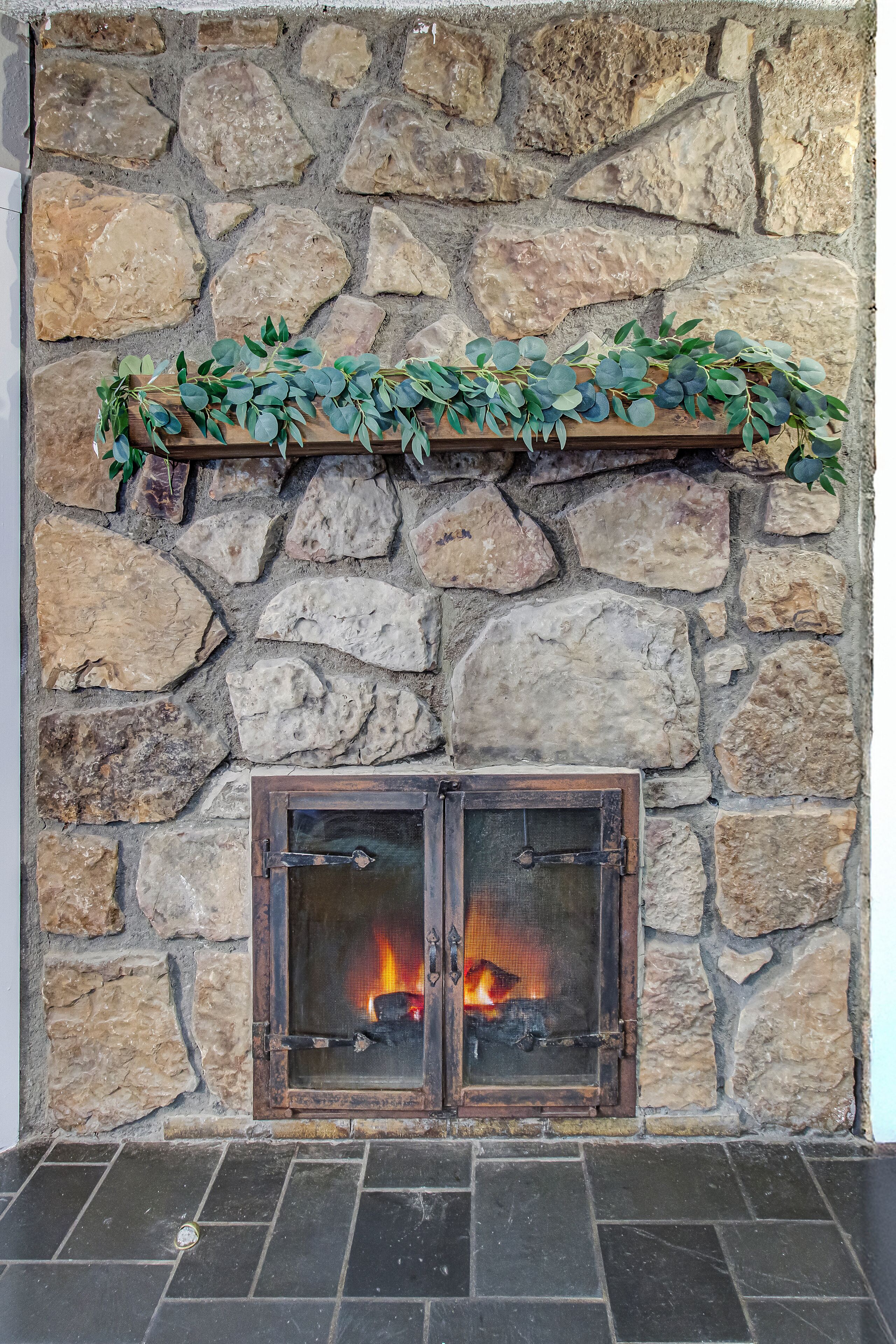 A stone fireplace with a wooden mantel and a fire burning inside.