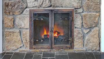 A stone fireplace with a wooden mantel and a fire burning inside.