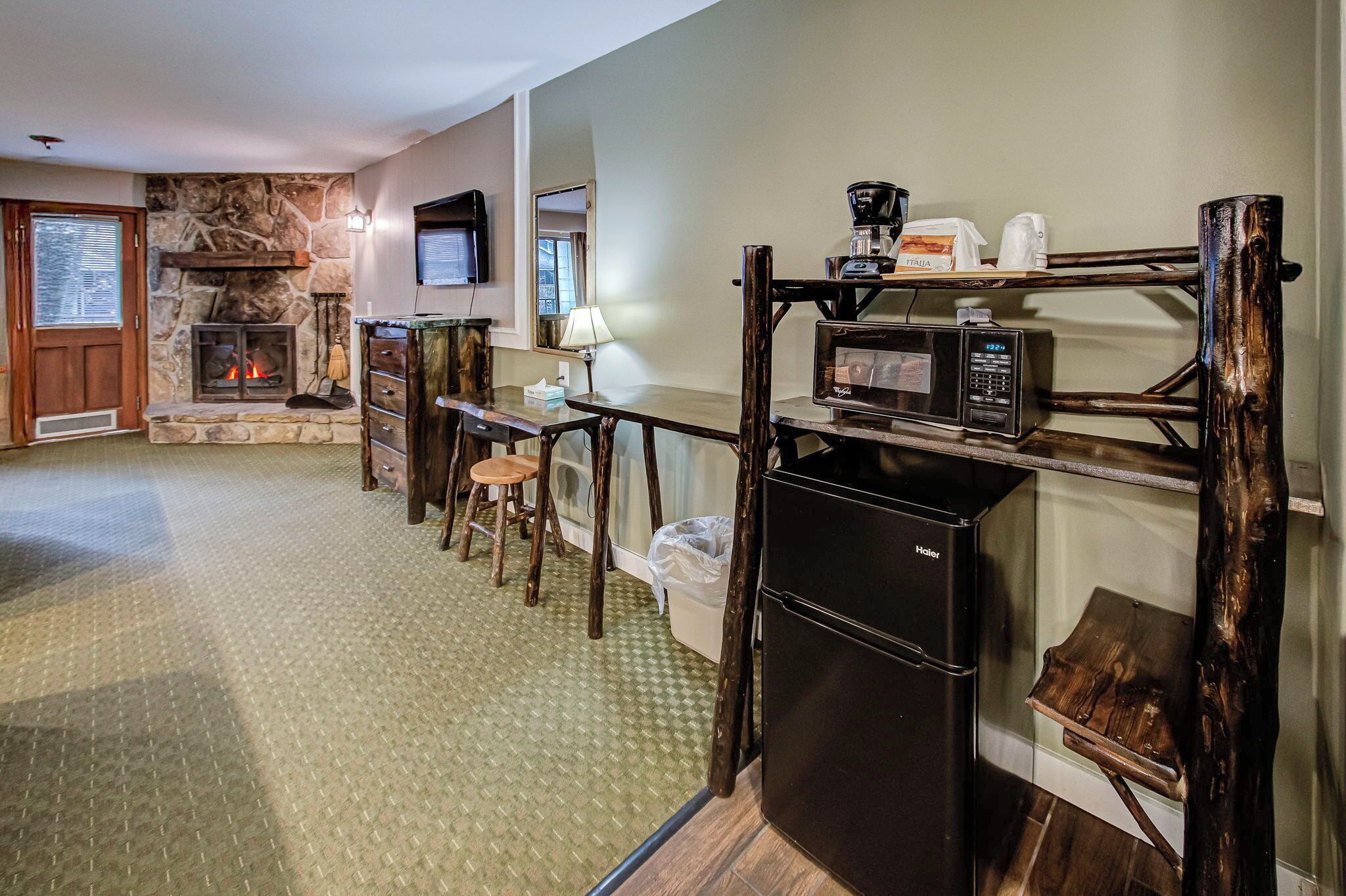 A cozy living room with a stone fireplace, a wooden table with chairs, a coffee maker, a microwave, and a refrigerator.