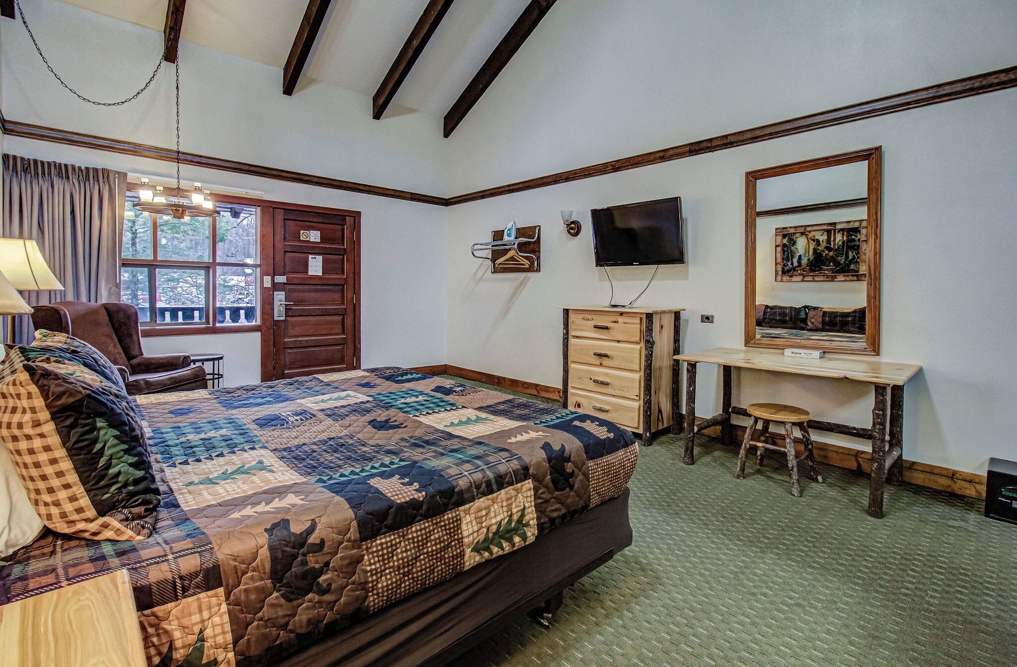 A bedroom with a large bed, a desk, a chair, a TV, and a window with curtains.