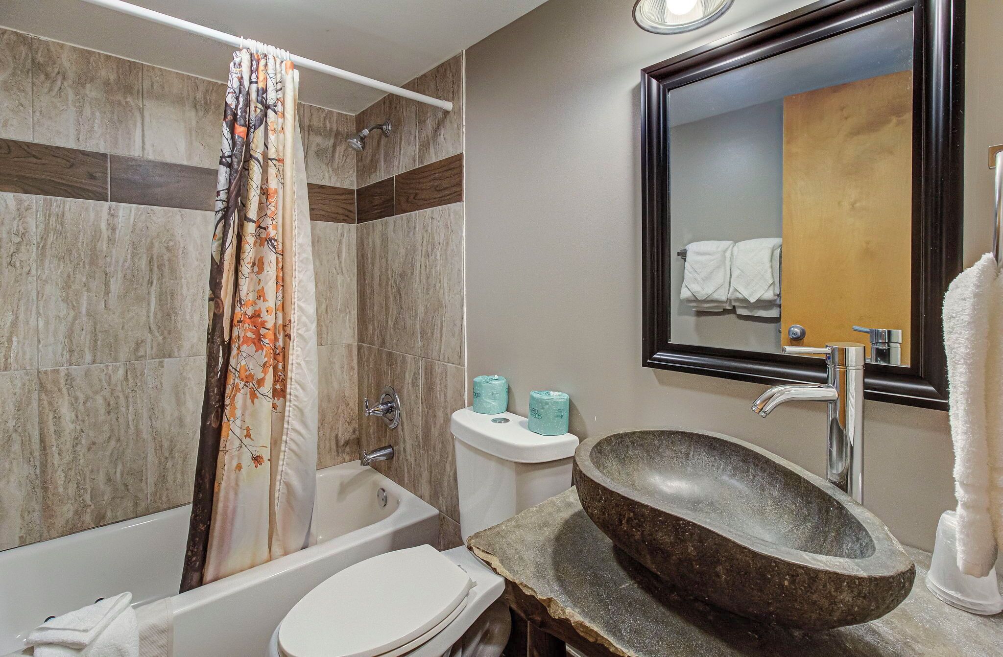 A bathroom with a bathtub, toilet, and sink with a stone basin.