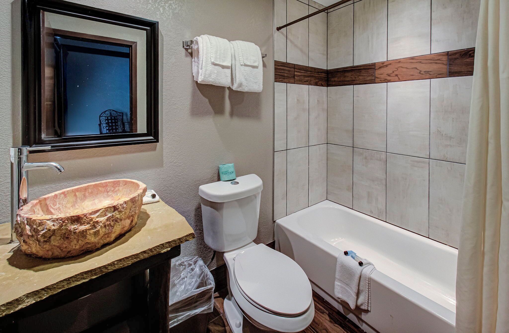 A bathroom with a wooden vanity, a large sink, a toilet, and a bathtub.