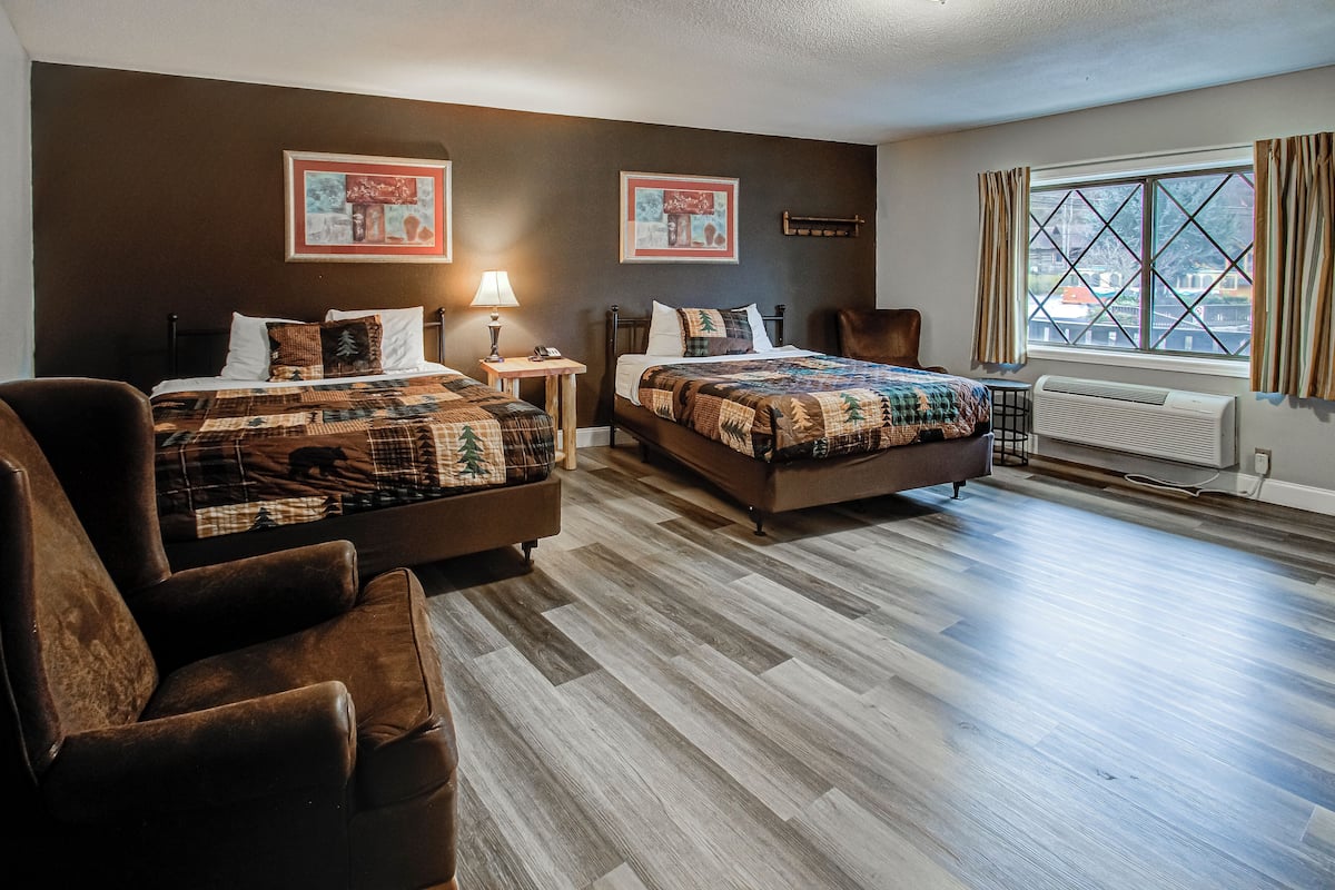 A hotel room with two beds, a large window with curtains, a wooden floor, and a chair.