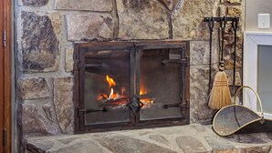 A stone fireplace with a fire, a wooden shelf above it, and a lantern on the wall. - Brookside Lodge (Gatlinburg)