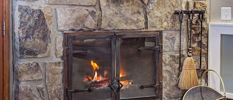 A stone fireplace with a fire, a wooden shelf above it, and a lantern on the wall.