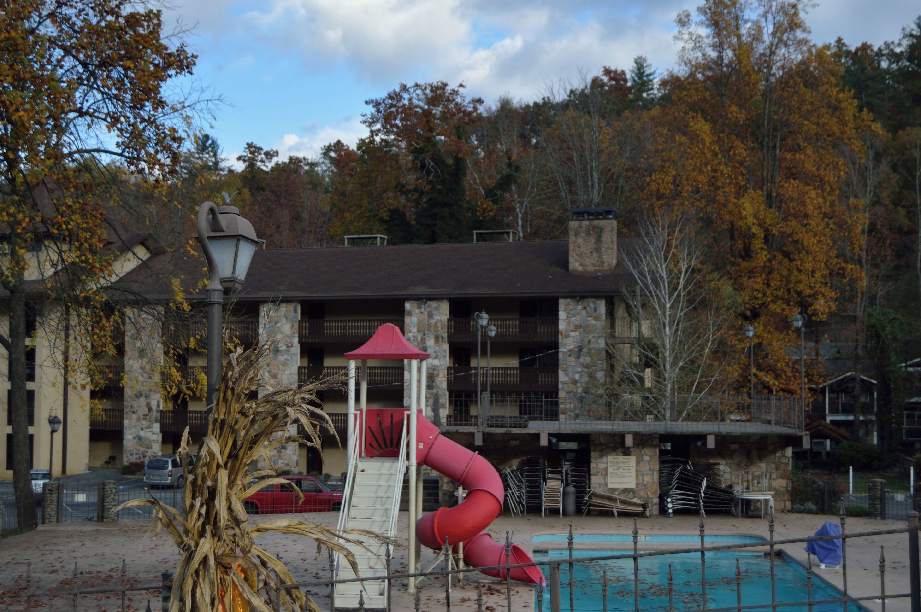 A playground with a red slide and a small pavilion, a swimming pool, and a building with balconies in the background.
