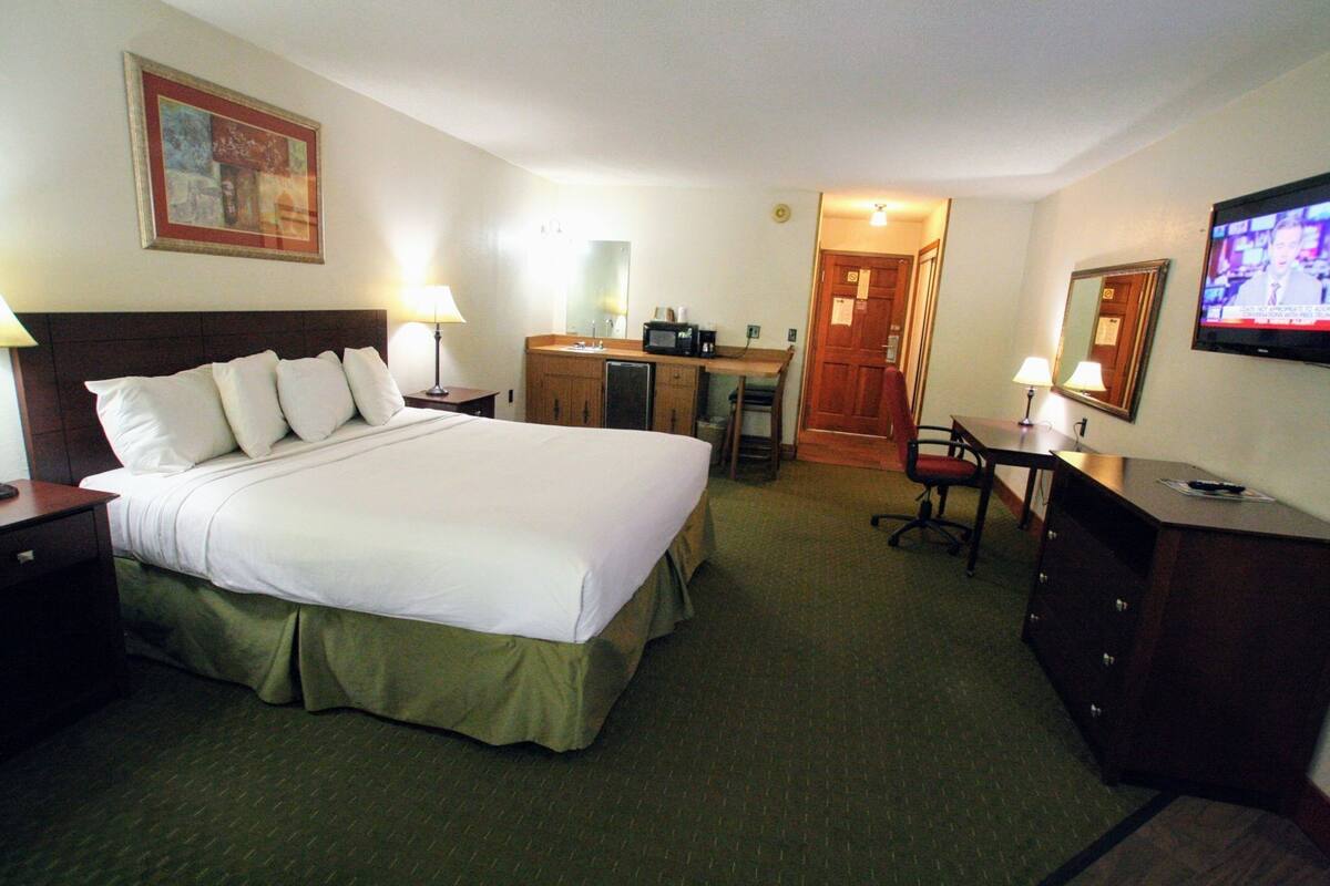 A hotel room with a large bed, a desk, a chair, a television, and a mirror.