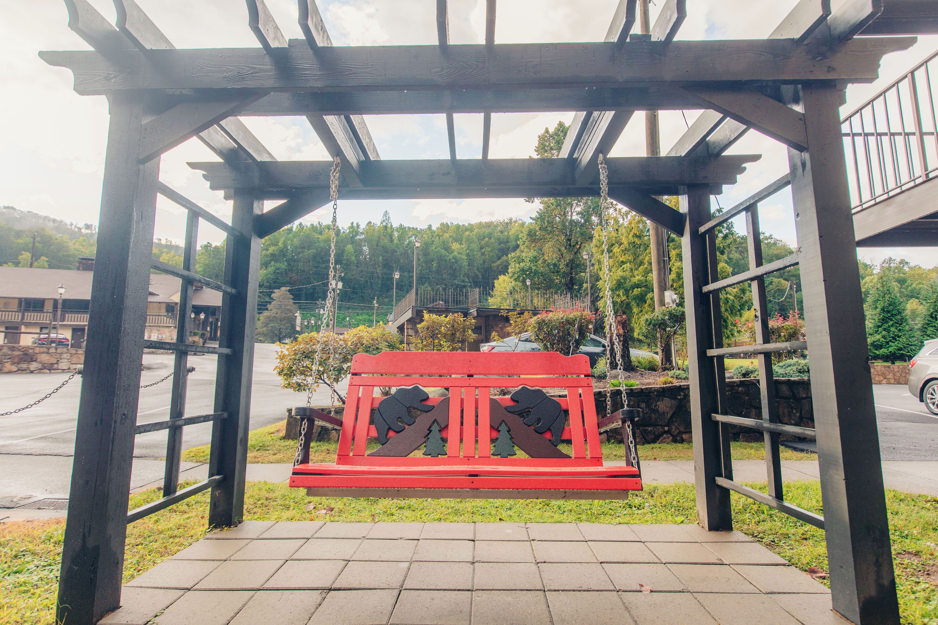 A wooden pergola with a red bench underneath, surrounded by a paved walkway.
