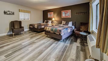 Habitación de hotel con dos camas, una silla, una mesita, un calefactor y una ventana con cortinas.