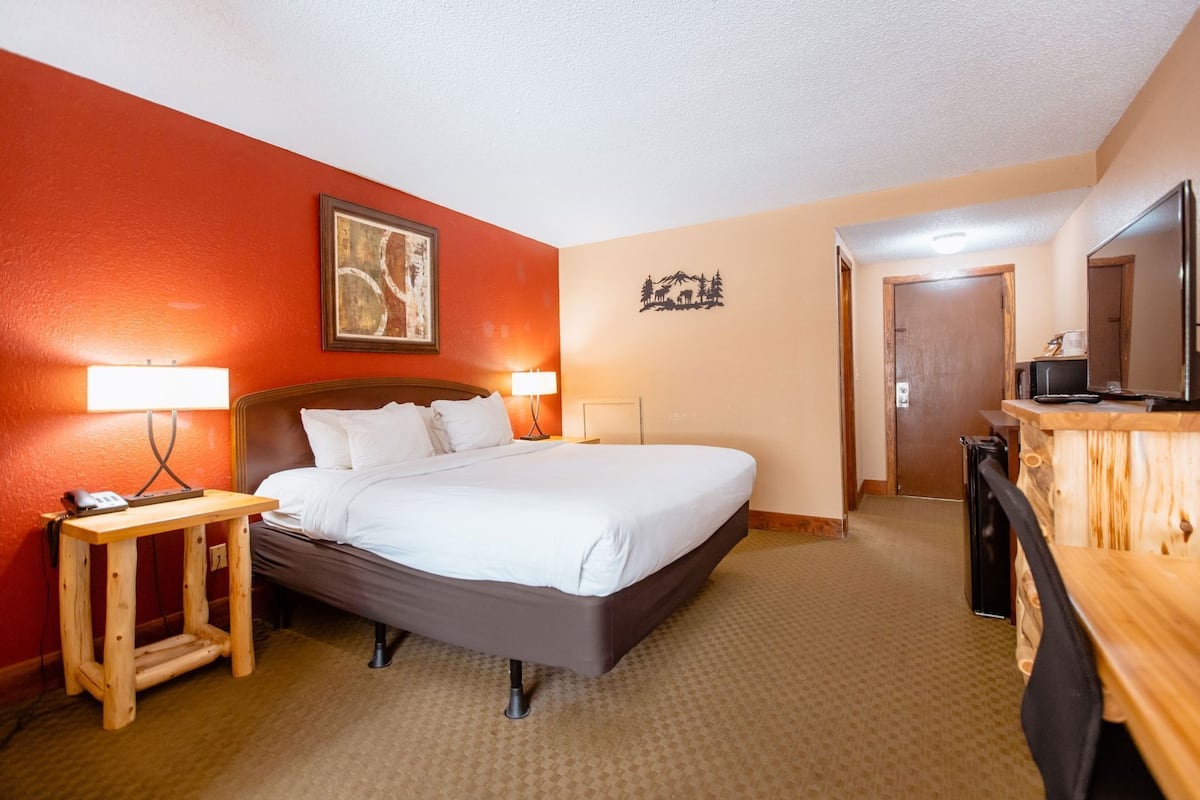A hotel room with a bed, bedside tables, a desk, a television, and a door leading to another room.