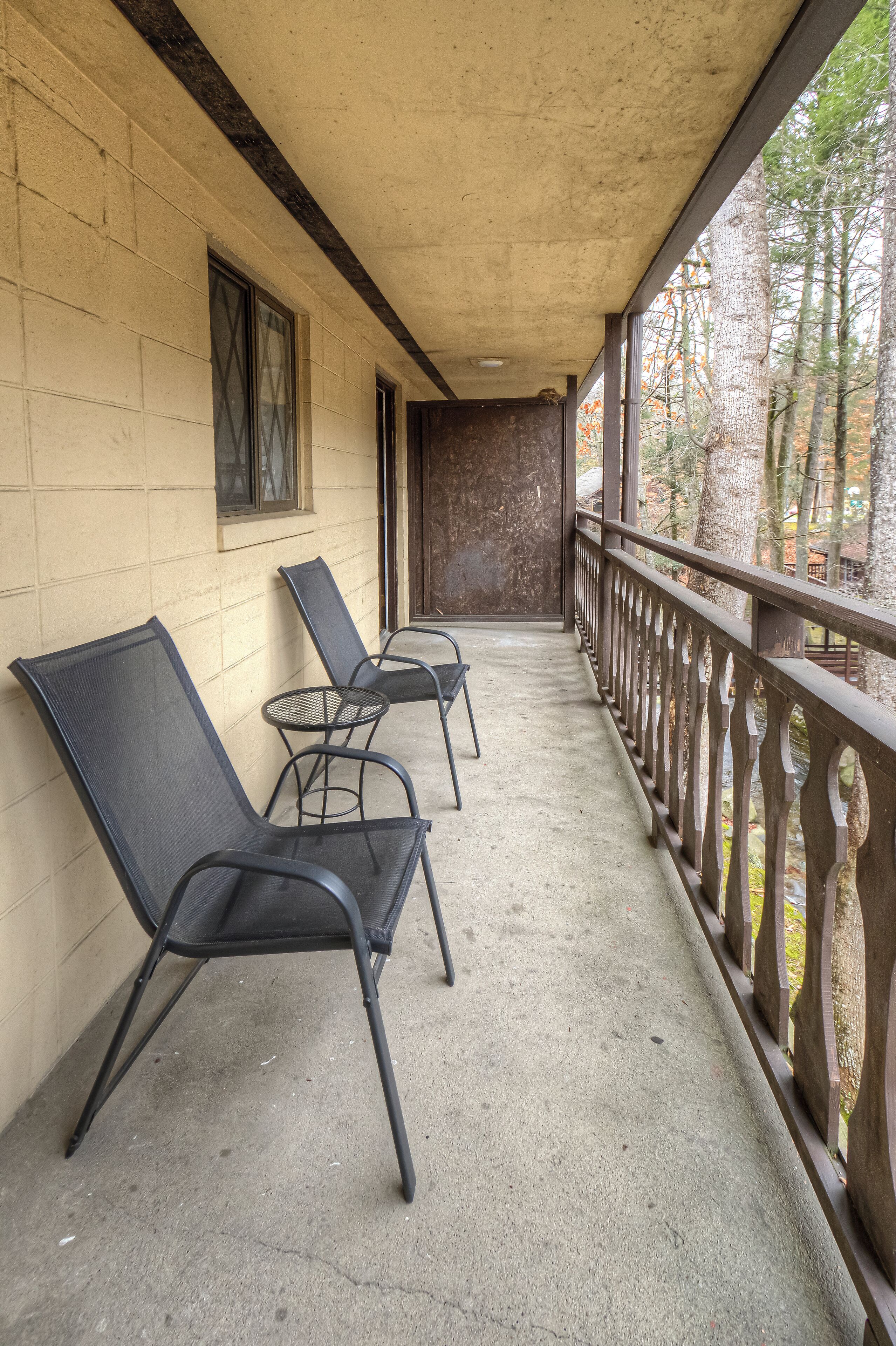 A covered porch with two black lounge chairs and a small round table.